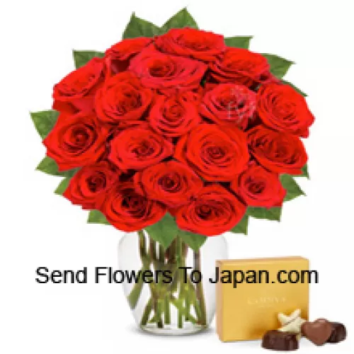 25 Trandafiri roșii cu câteva frunze de ferigă într-o vază de sticlă însoțiți de o cutie de ciocolată importată
