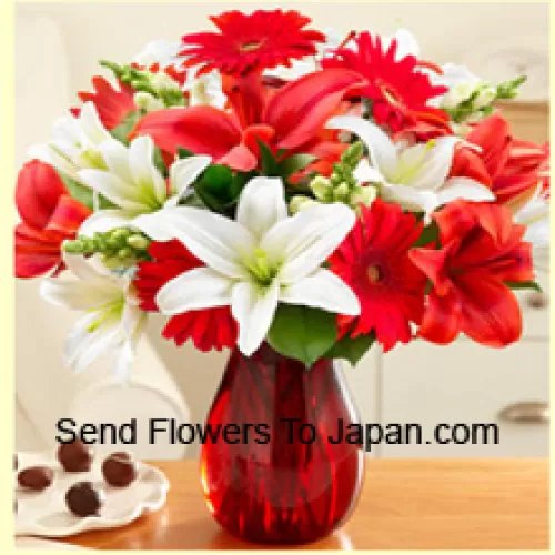 Красные герберы, белые лилии, красные лилии и другие разноцветные цветы красиво уложены в стеклянной вазе