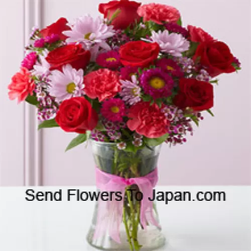 Punaiset ruusut, punaiset neilikat ja muut erilaiset kukat kauniisti aseteltuna lasimaljakkoon