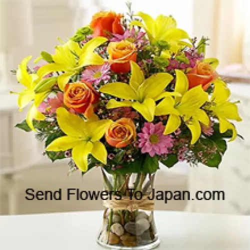 Keltaisia liljoja, oransseja ruusuja ja vaaleanpunaisia gerberoita kausitäytteillä lasimaljakossa